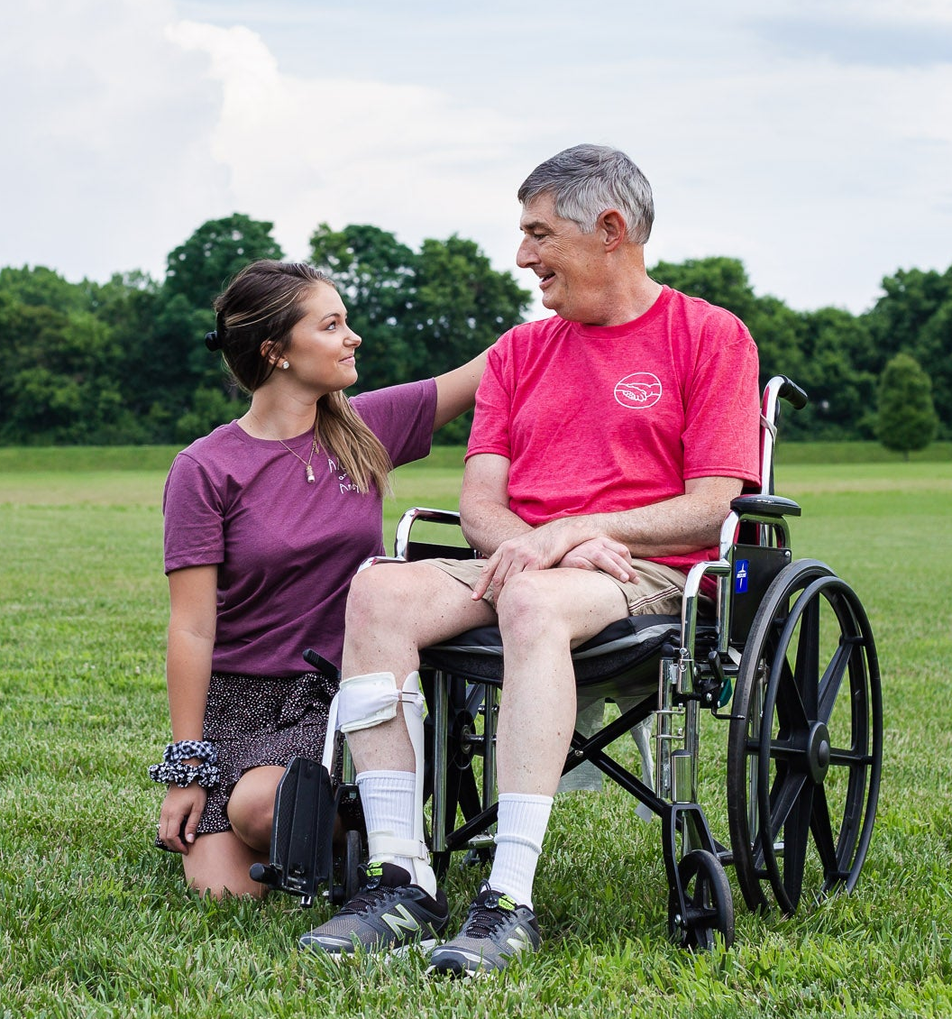 Andy in a wheelchair and Sophie kneeling on grass in a park